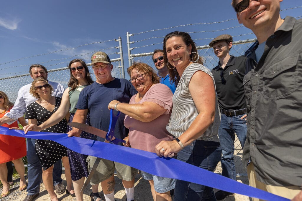 blue ribbon cutting with employees smiling